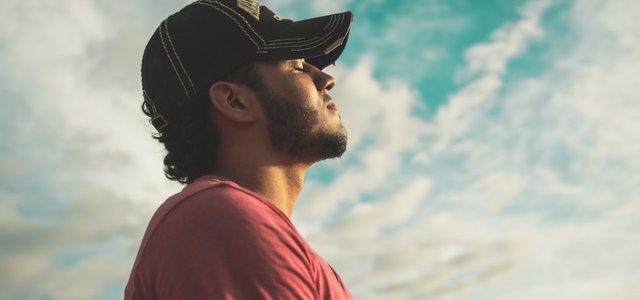 man with eyes closing breathing slow with clouds behind