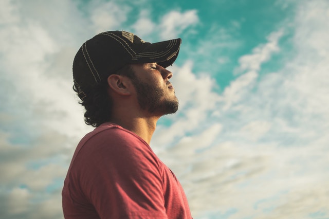 man with eyes closing breathing slow with clouds behind