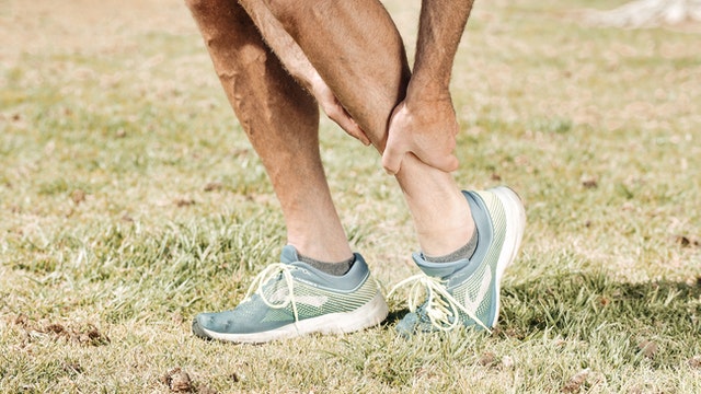 the lower part of a man's legs, grabbing his injured ankle with one hand