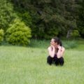 woman squatting in grass, looking confused to the side
