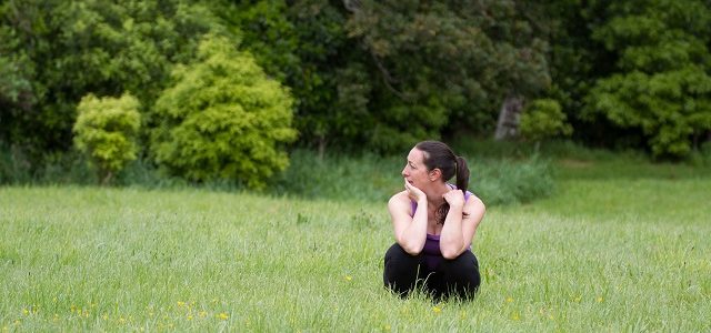 woman squatting in grass, looking confused to the side