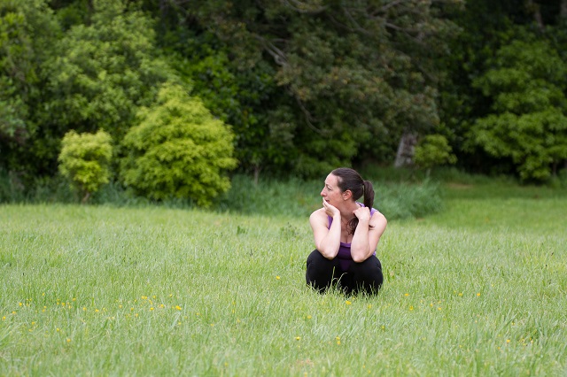woman squatting in grass, looking confused to the side