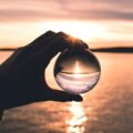 photo of a person holding a glass globe reflecting the ocean at sunset