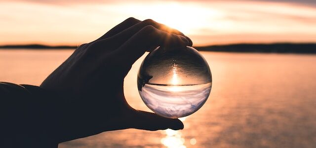 photo of a person holding a glass globe reflecting the ocean at sunset